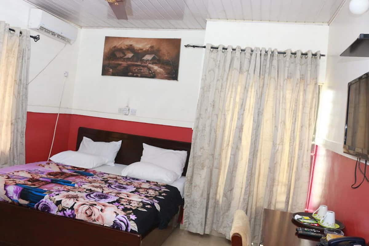 Un dormitorio con una cama, cortinas, un cuadro y una mesa con objetos.