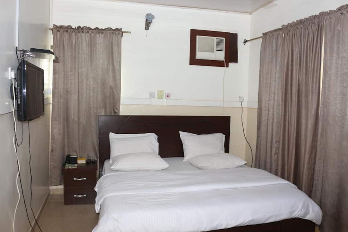 Una habitación de hotel con una cama, cortinas, un televisor y una mesita con un libro.