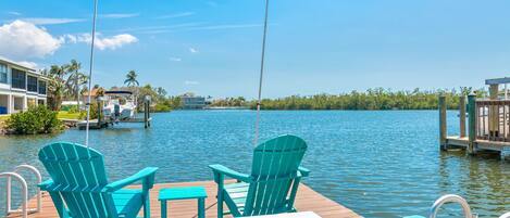 A wooden dock with two green Adirondack chairs and a small table.