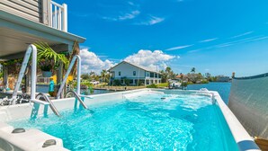 Ein Swimmingpool mit klarem, blauem Wasser, eine Poollandschaft mit einer Liege und ein Haus im Hintergrund.