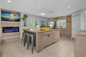 A modern kitchen with a large island, bar stools, a built-in refrigerator, and a TV mounted on the wall. - Latitude 26 Waterfront Boutique Resort - Bonita Springs (Bonita Springs)