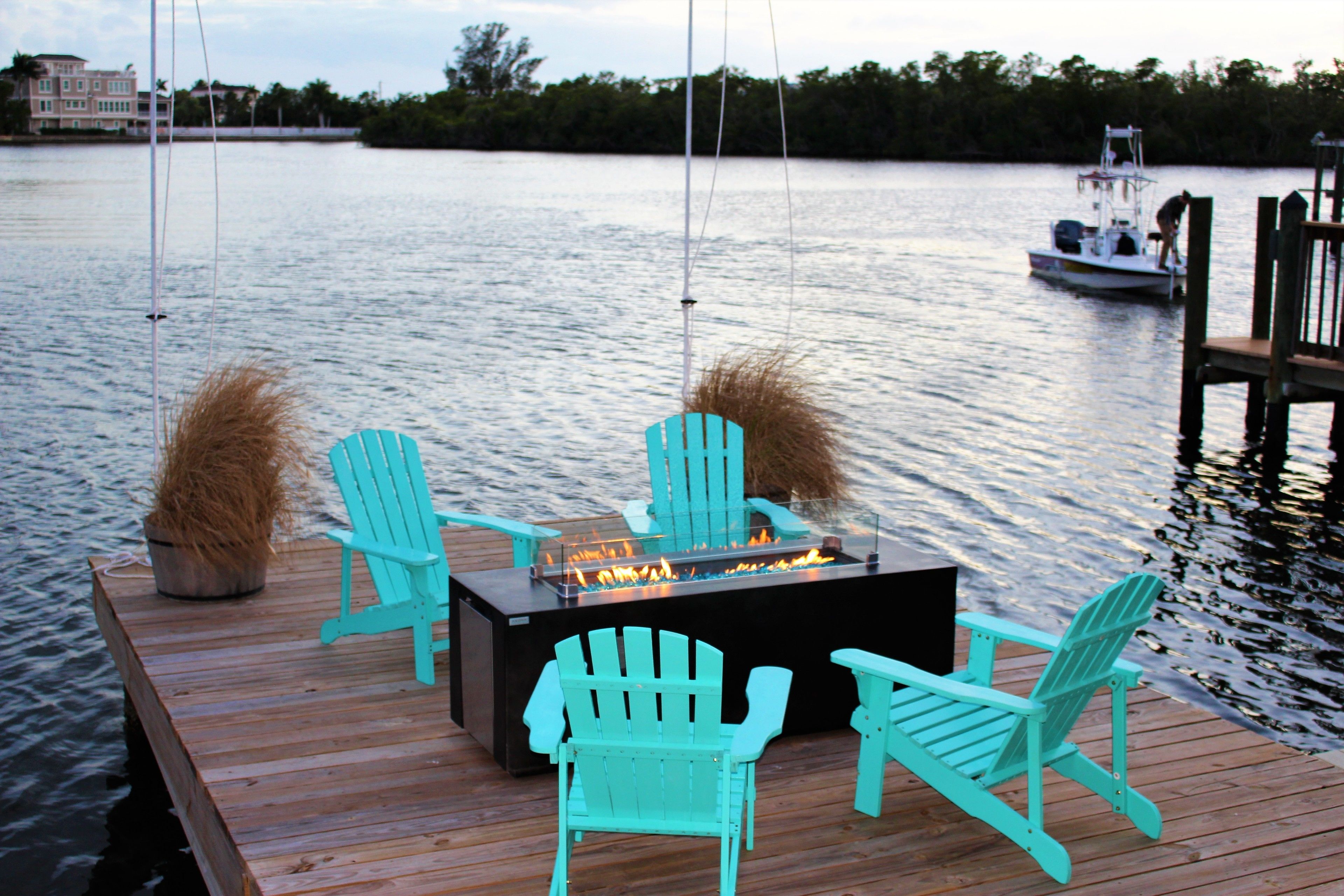 A wooden dock with a fire pit and two Adirondack chairs.