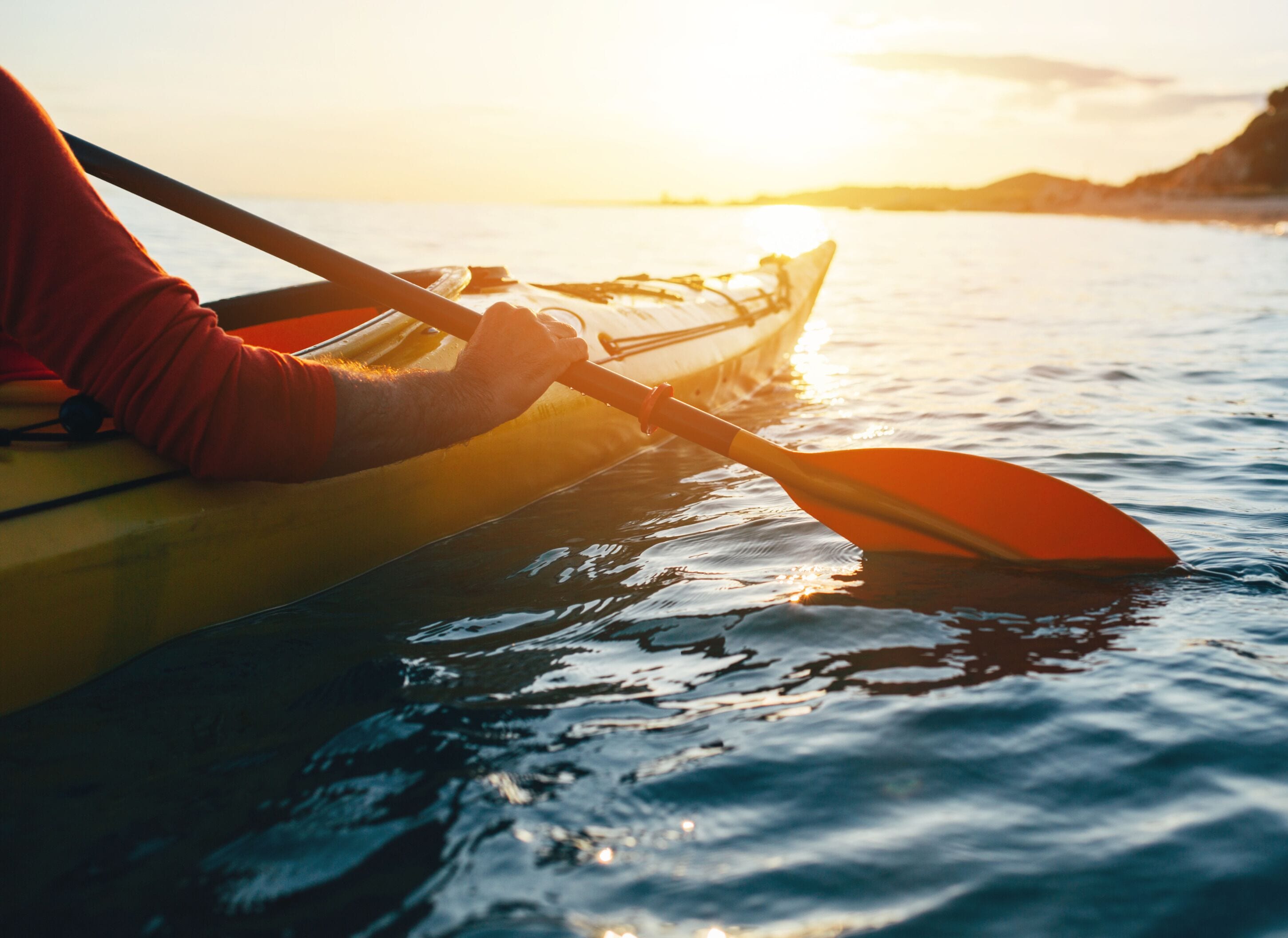A person in a yellow kayak on calm water during sunset.