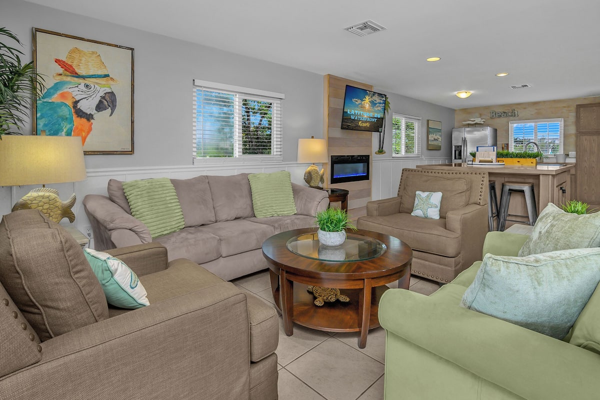 A living room with a sofa set, a coffee table, a television, and a kitchen area with a refrigerator.