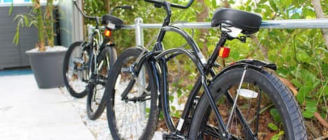 A row of bicycles parked against a metal railing, with a concrete path and greenery in the background.