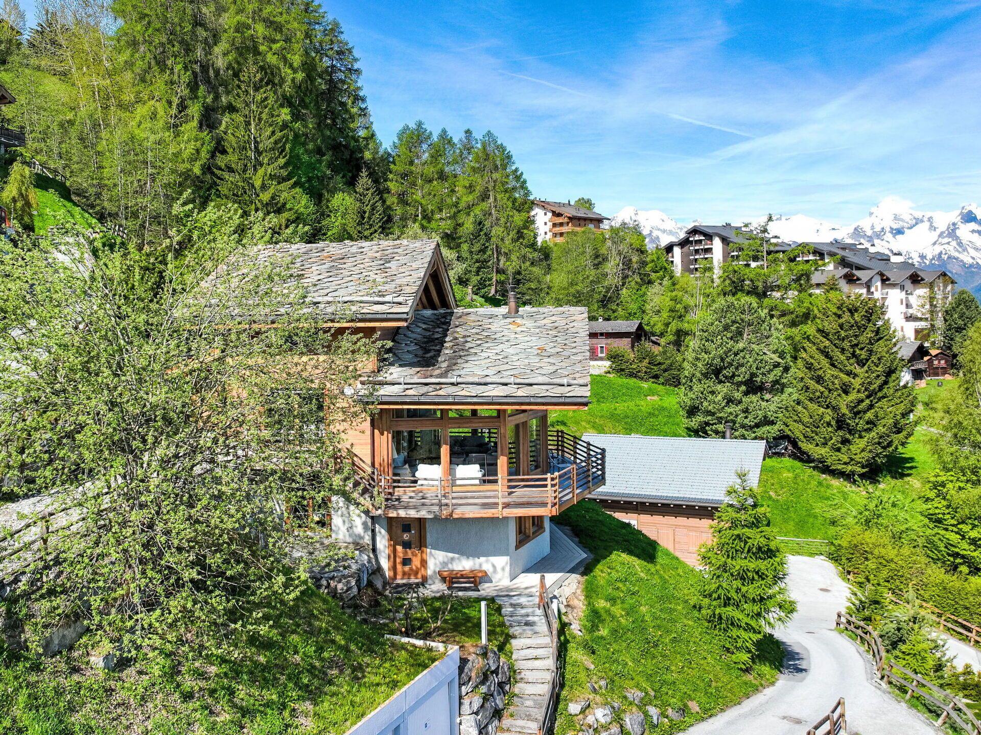 Een chalet met een balkon, omringd door weelderig groen en een kronkelende weg.