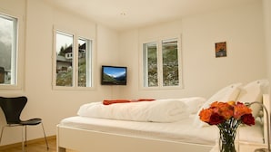 Une chambre à coucher moderne avec un lit, un téléviseur fixé au mur et une fenêtre donnant sur un paysage enneigé.