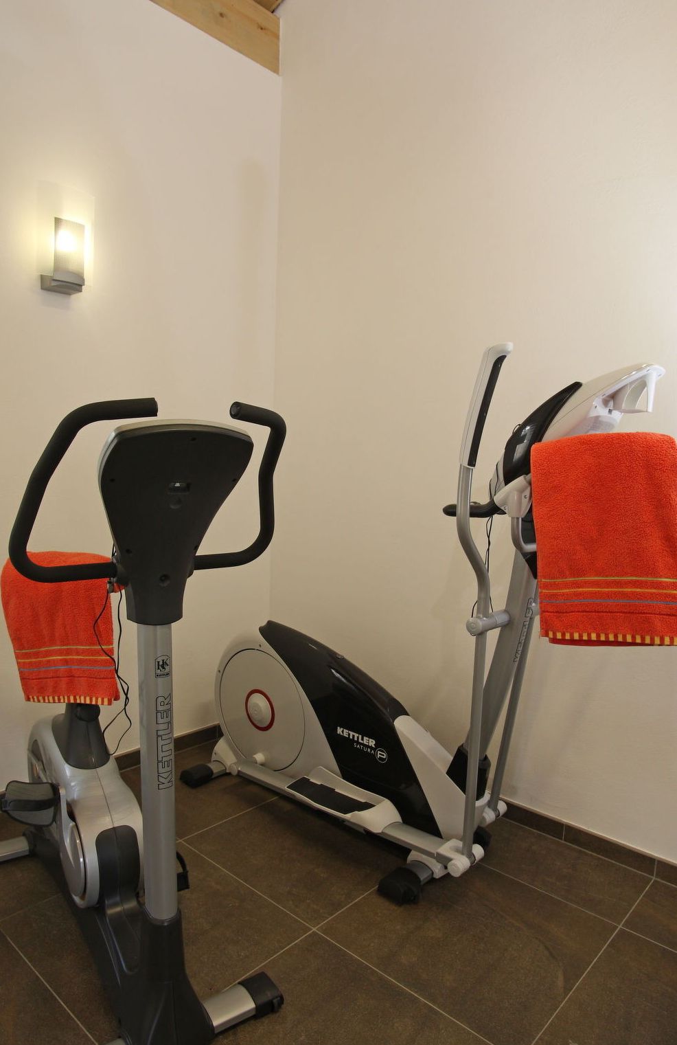 An exercise machine with a towel draped over it, a wall-mounted light, and a tiled floor.