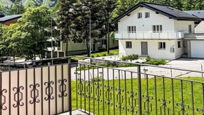 A residential area with a white house, a paved pathway, and a metal fence. - Beautiful apartment for 2 guests with WIFI, hot tub, TV and terrace (Leukerbad)