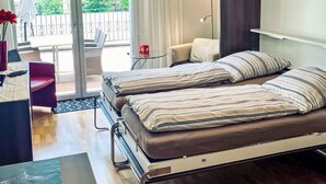 A modern bedroom with a bed, a desk, and a chair. There is a balcony with a view of greenery. - Beautiful apartment for 2 guests with WIFI, hot tub, TV and terrace (Leukerbad)