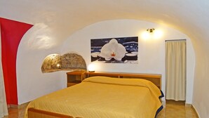 A bedroom with a bed, a stone wall, a painting of an orchid, and a red accent wall.