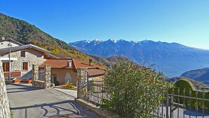 A stone building with a red-tiled roof, a paved street, and a mountain backdrop.