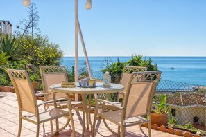 Un patio con una mesa y sillas redondas, con vistas a un mar azul y despejado.