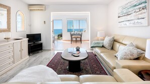 A modern living room with a sofa, coffee table, and TV. There is a view of the sea through large windows. - Polarsol 2 (Mijas)