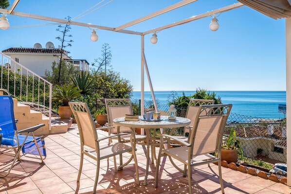 Un patio al aire libre con una mesa redonda y sillas, con vista al mar.