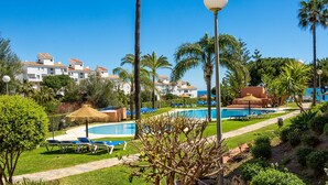 A pool area with lounge chairs, palm trees, and a clear blue sky. - Polarsol 2 (Mijas)