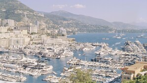 Un port de plaisance rempli de nombreux yachts et bateaux, entouré d’un paysage urbain avec des bâtiments et des collines en arrière-plan.