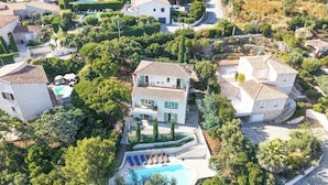 Un quartier résidentiel avec une grande maison dotée d’une piscine, de nombreux balcons et d’une végétation luxuriante.