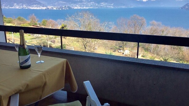 A table with a bottle and glasses, overlooking a scenic view of mountains and a body of water. - Thommy apartment in Stresa with  lake view (Stresa)