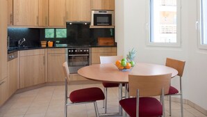 A modern kitchen with wooden cabinets, a black countertop, stainless steel appliances, and a dining area with a round table and red chairs. - Lovely apartment for 4 people with WIFI, hot tub, TV and balcony (Leukerbad)