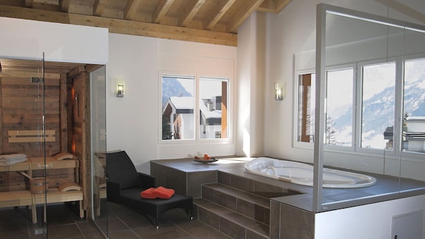Une salle de bain moderne avec un plafond en bois, une douche en verre, une chaise noire, un grand miroir et une vue sur les montagnes par les fenêtres.
