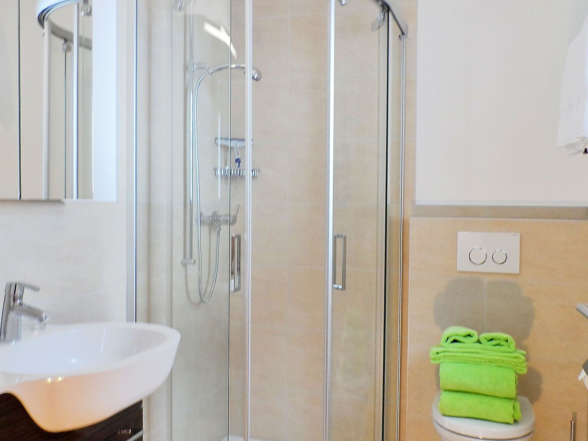 A bathroom with a glass-enclosed shower, a white sink, and a toilet with green towels.
