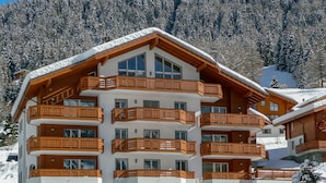 Un hôtel à plusieurs étages doté de balcons en bois, de grandes fenêtres et surplombant un paysage montagneux enneigé.