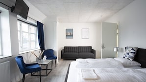 A hotel room with a bed, a sofa, a desk, a chair, and a window with curtains. - Hotel City (Holstebro)