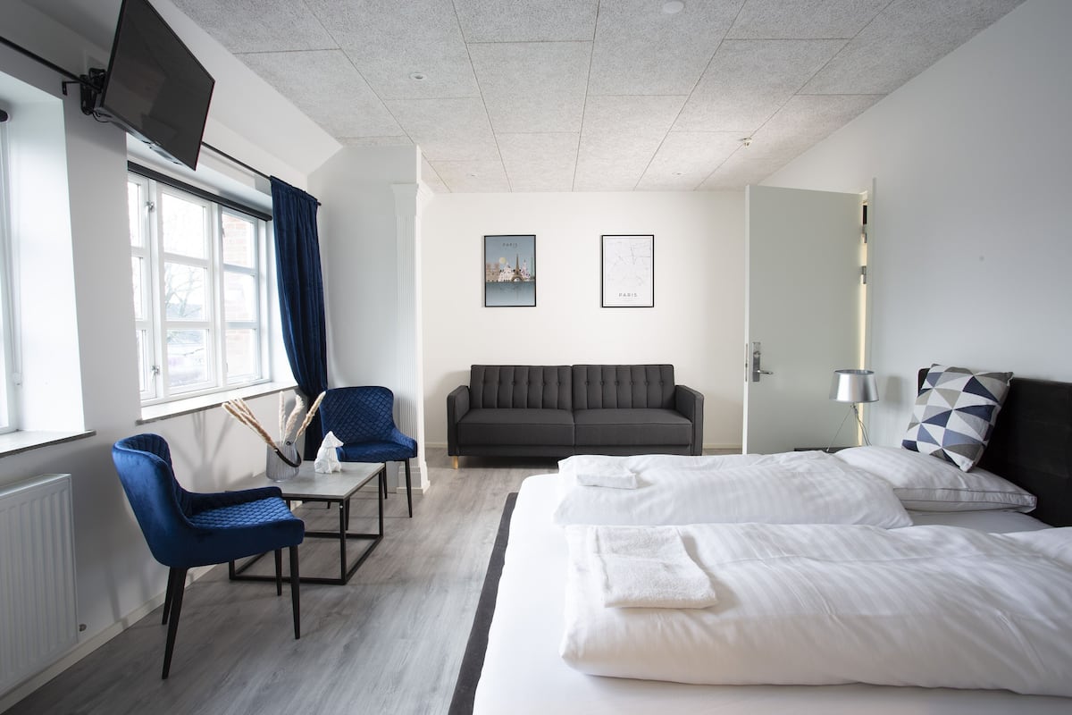 A hotel room with a bed, a sofa, a desk, a chair, and a window with curtains.