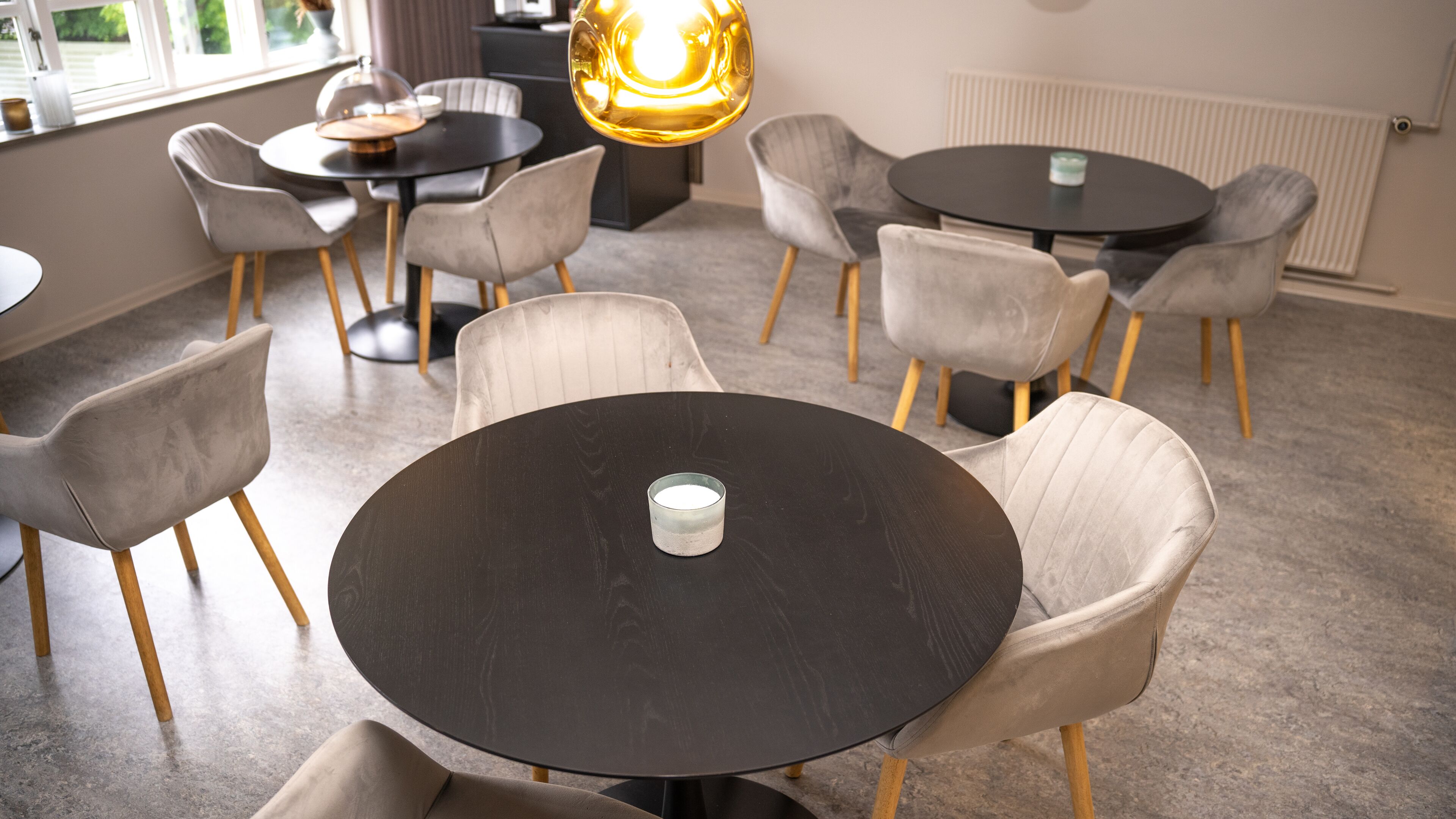 A modern dining area with round tables and cushioned chairs, a glass candle holder, and a large pendant light.