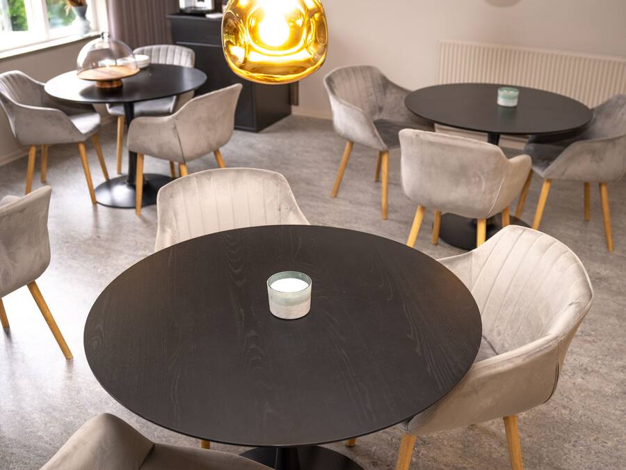 A modern dining area with round tables and cushioned chairs, a glass candle holder, and a large pendant light.