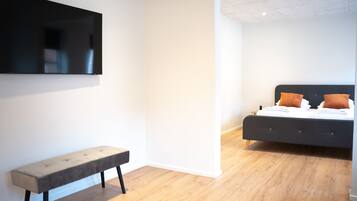 A modern bedroom with a bed, bench, and a flat-screen TV mounted on the wall.