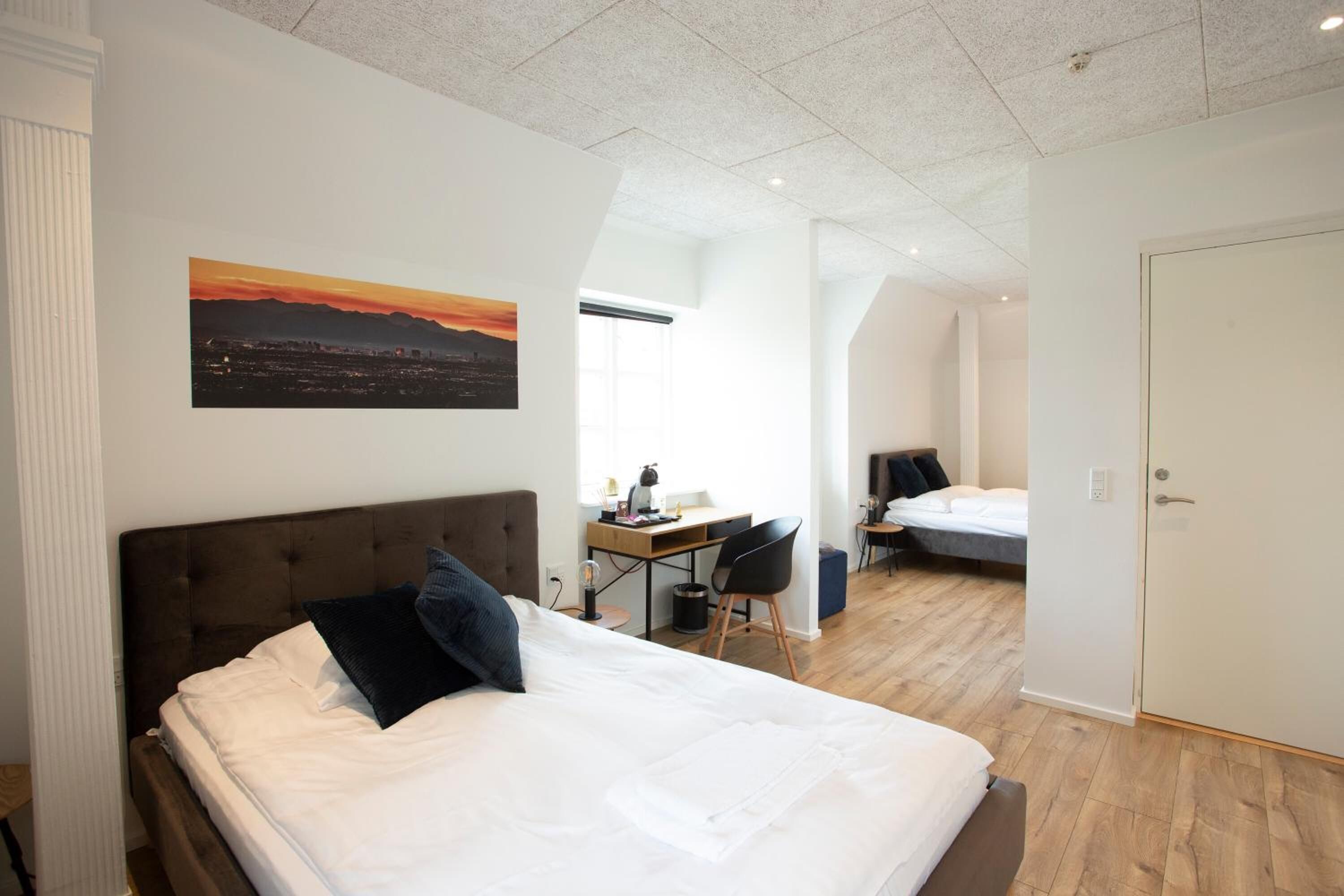 Een moderne hotelkamer met een groot bed, een bureau en een stoel. Er hangt een schilderij aan de muur en bevindt zich een deur aan de rechterkant.