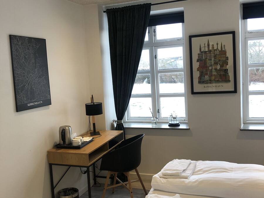 Una habitación de hotel con una cama, un escritorio con una silla, una cafetera y un cuadro enmarcado con una vista urbana.