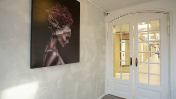 Un pasillo con una obra de arte grande enmarcada en la pared y una puerta blanca con paneles de vidrio.