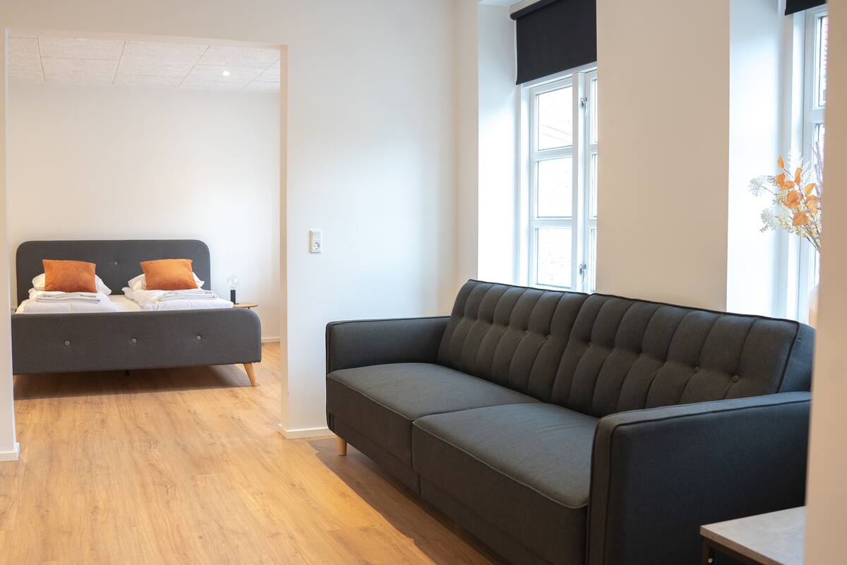 A modern bedroom with a bed, a grey sofa, and a window with a view.