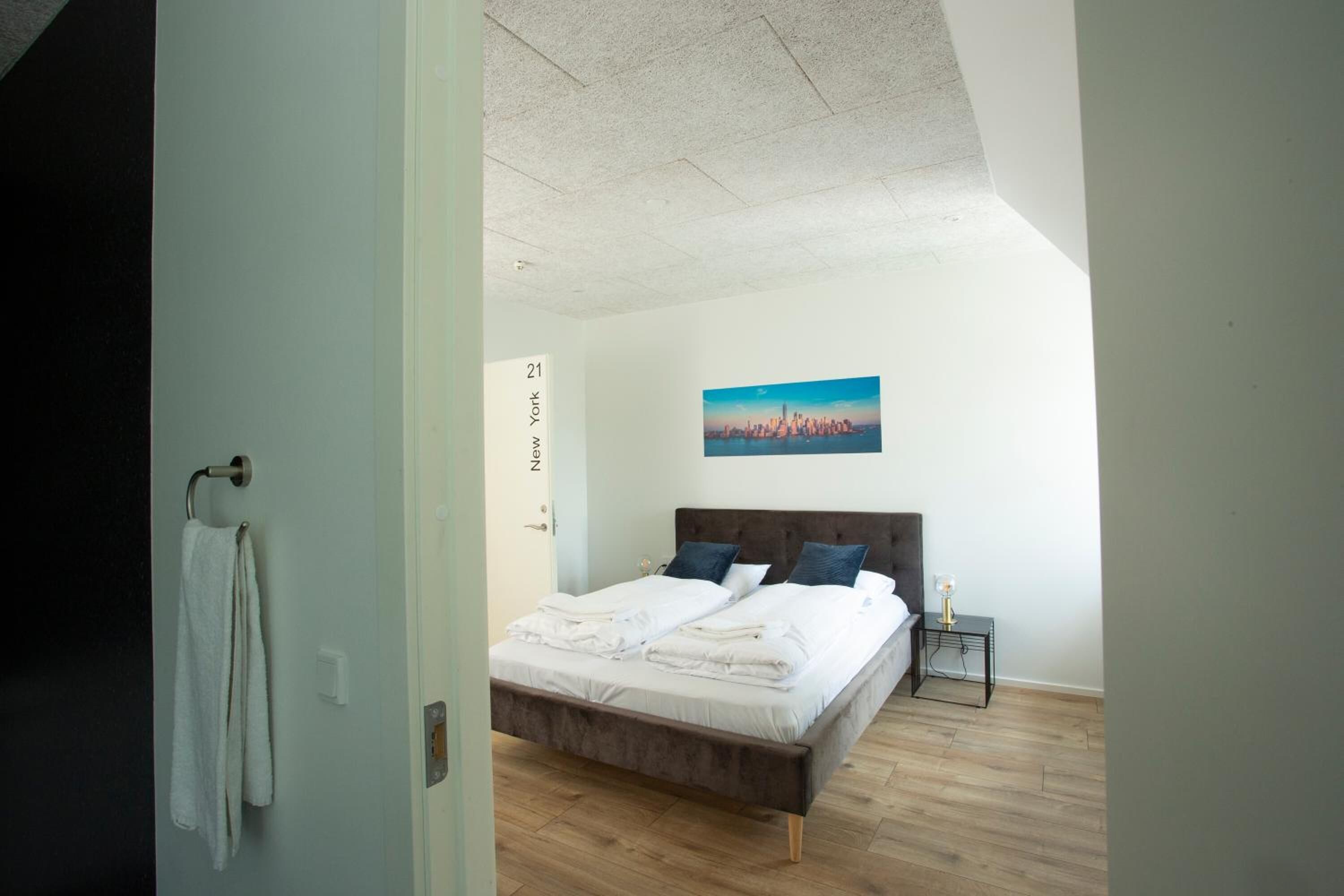 A bedroom with a bed, a painting of a cityscape, and a nightstand with a lamp.