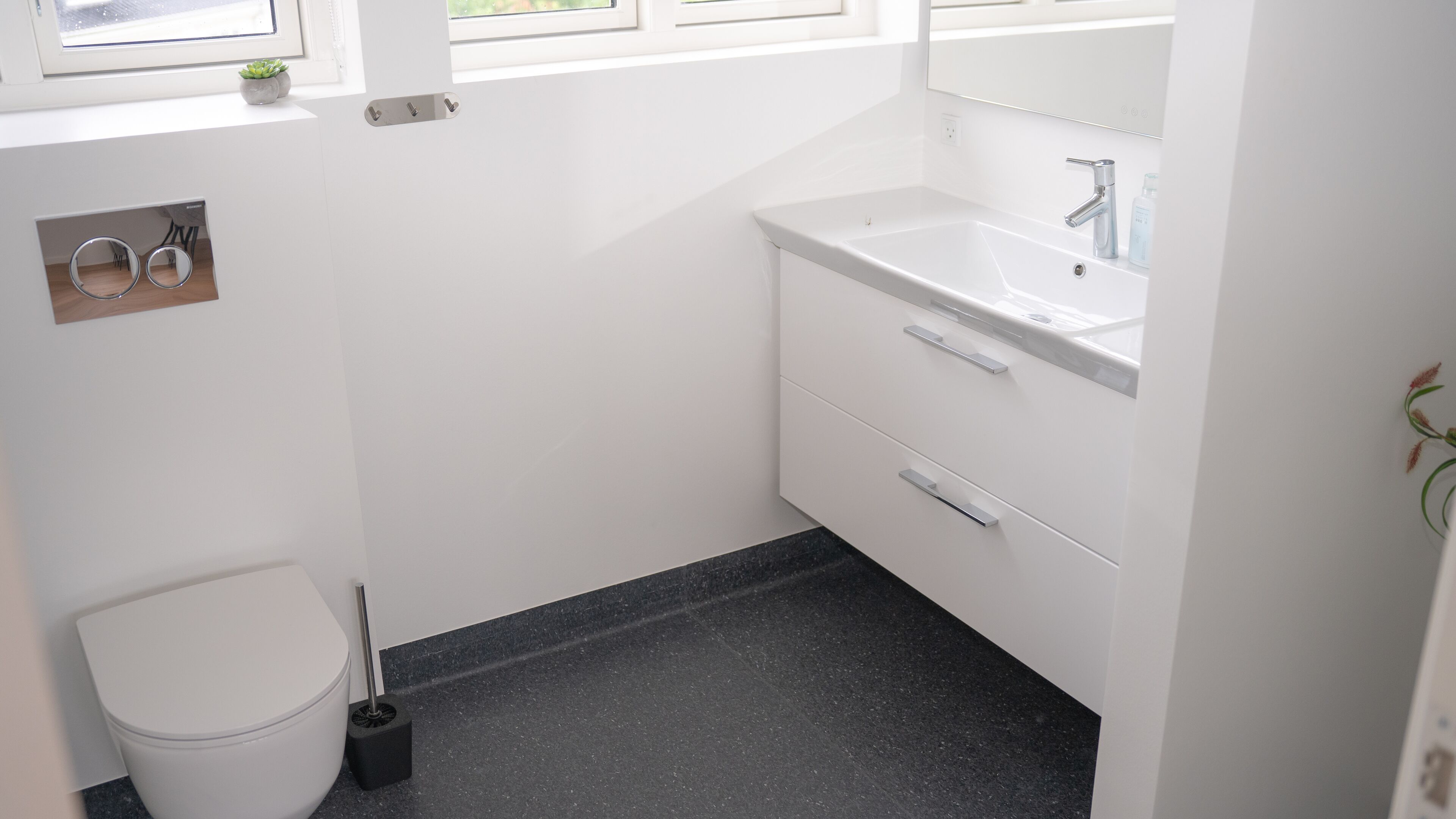 A bathroom with a white toilet, a sink with a mirror, and a black floor.