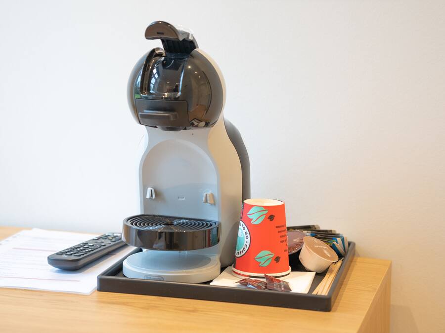 A coffee machine on a table with a remote control, a cup, and some food containers.