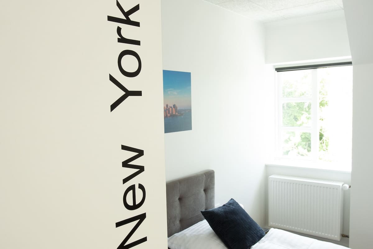 A hotel room with two beds, a view of the city, and a door labeled "21 New York".