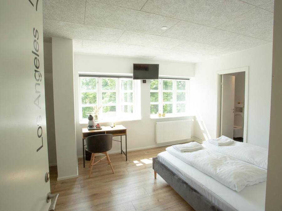 A bedroom with a bed, a desk, a chair, and a TV mounted on the wall.