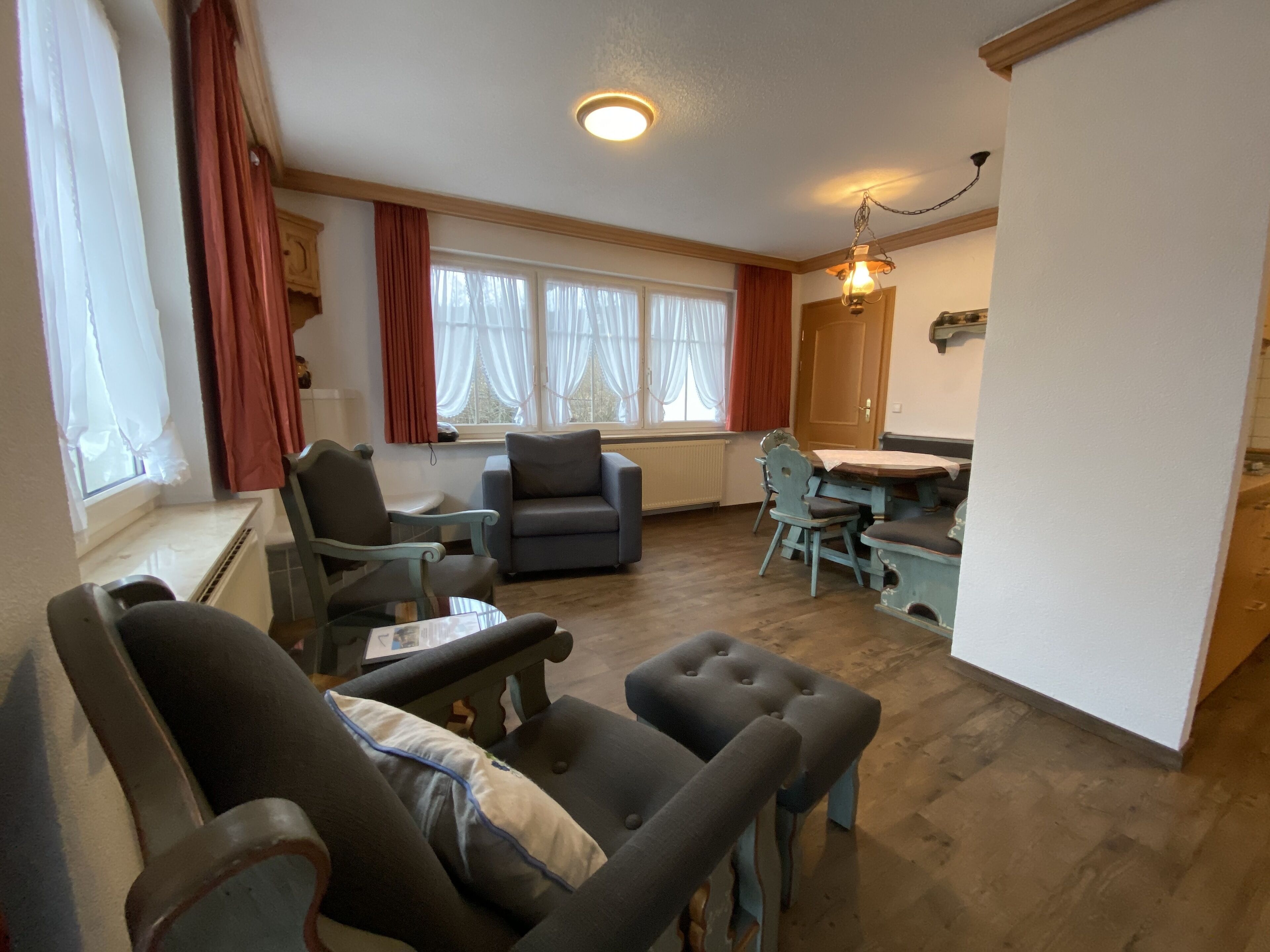 Een woonkamer met een eethoek, met een bank, fauteuils, een tafel en een kroonluchter.