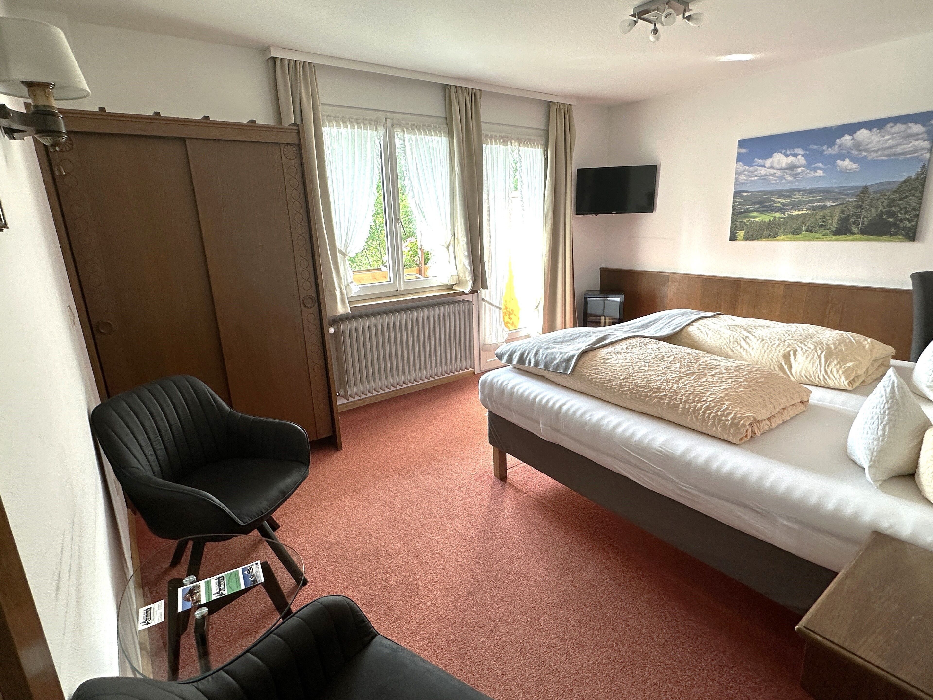 Ein Hotelzimmer mit Bett, Stuhl, Fernseher und einem Fenster mit Vorhängen.