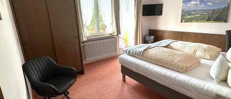 Une chambre d’hôtel avec un lit, une chaise, une télévision et une fenêtre avec des rideaux.