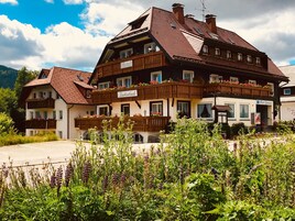 A traditional multi-story hotel with balconies, a sign indicating it is a hotel, and a view of the surrounding greenery.