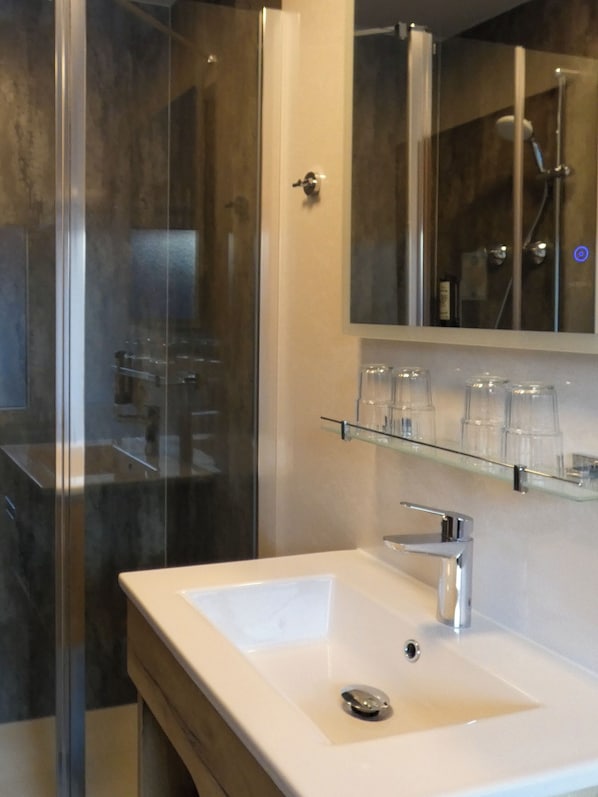 Un baño moderno con cabina de ducha de vidrio, un lavamanos blanco con un solo grifo y un espejo sobre el lavamanos.