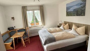 A hotel room with a bed, a desk with a chair, a radiator, and a window with curtains.