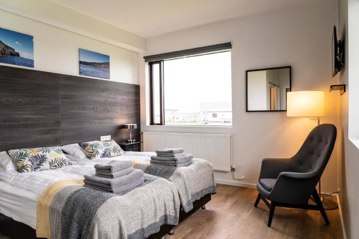 A hotel room with two beds, a chair, a window with a view, and a wall-mounted TV.