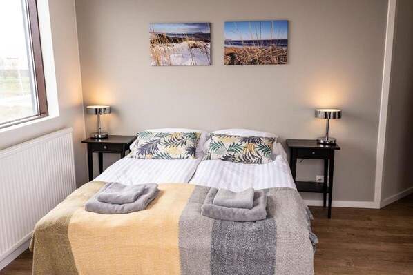 Una cama doble con dos almohadas, una mesita de noche con lámpara y dos cuadros colgados en la pared.