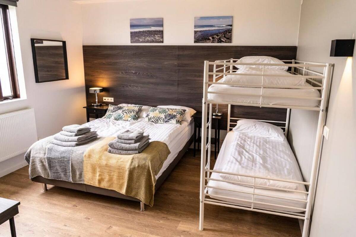 A bedroom with a bunk bed, a single bed, a nightstand with a lamp, and two framed pictures on the wall.